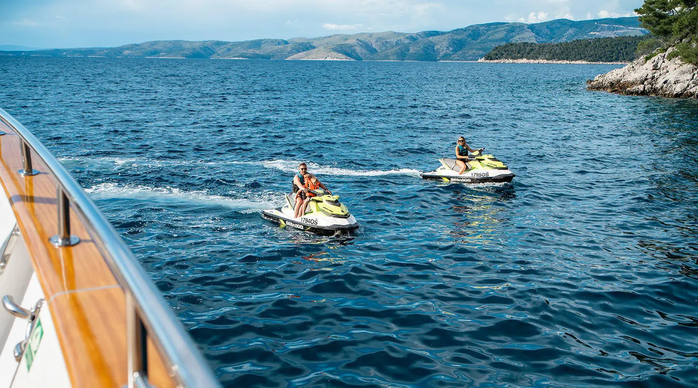 Dalmatino yacht at sea with two jet skis riding small waves at sunset