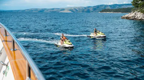 Dalmatino yacht at sea with two jet skis riding small waves at sunset