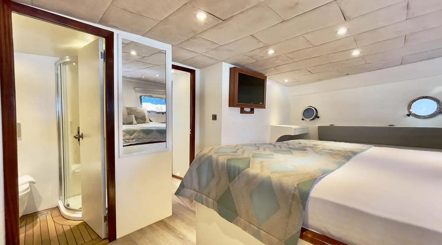 Sunset-lit yacht cabin with bed, seating, TV, and doorway to deck