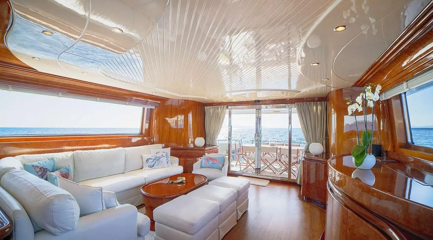 Interior of a yacht saloon with white seating, wooden cabinets, and large windows