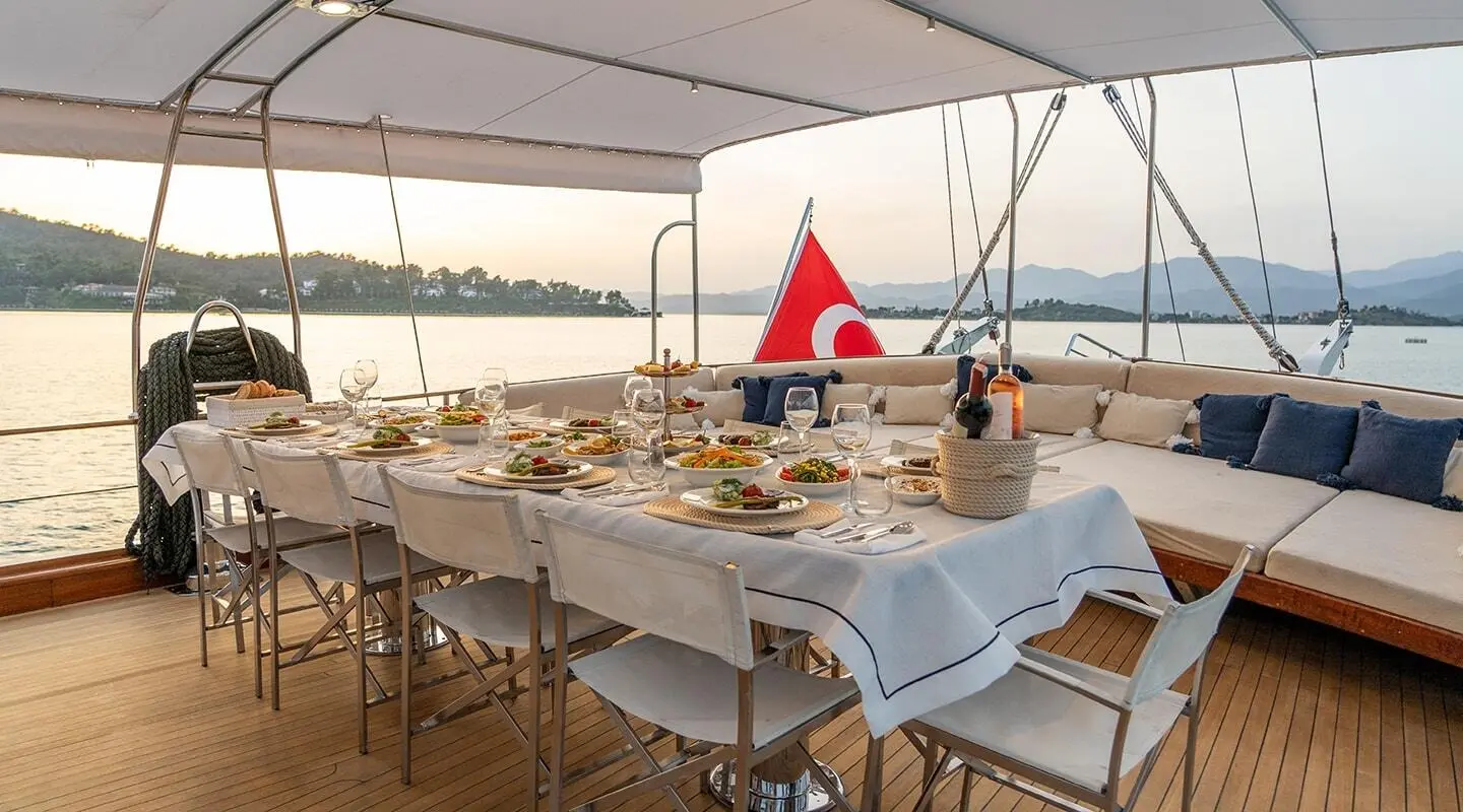 Aboard Happy Days gulet, aft deck setup with dining tables and chairs under shade, sunset view