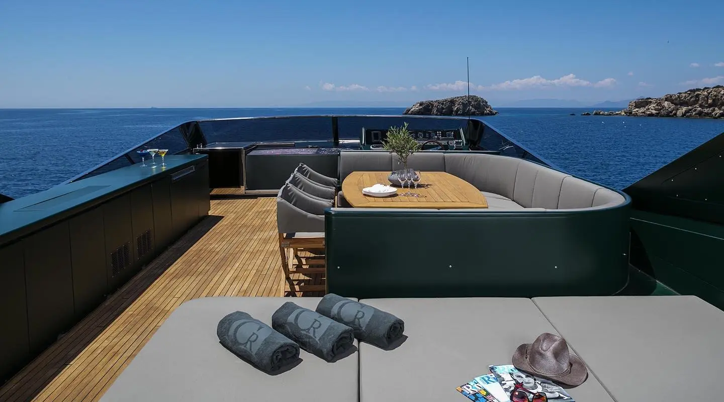 Luxury yacht deck dining area with seating, table, ocean view, and a distant yacht