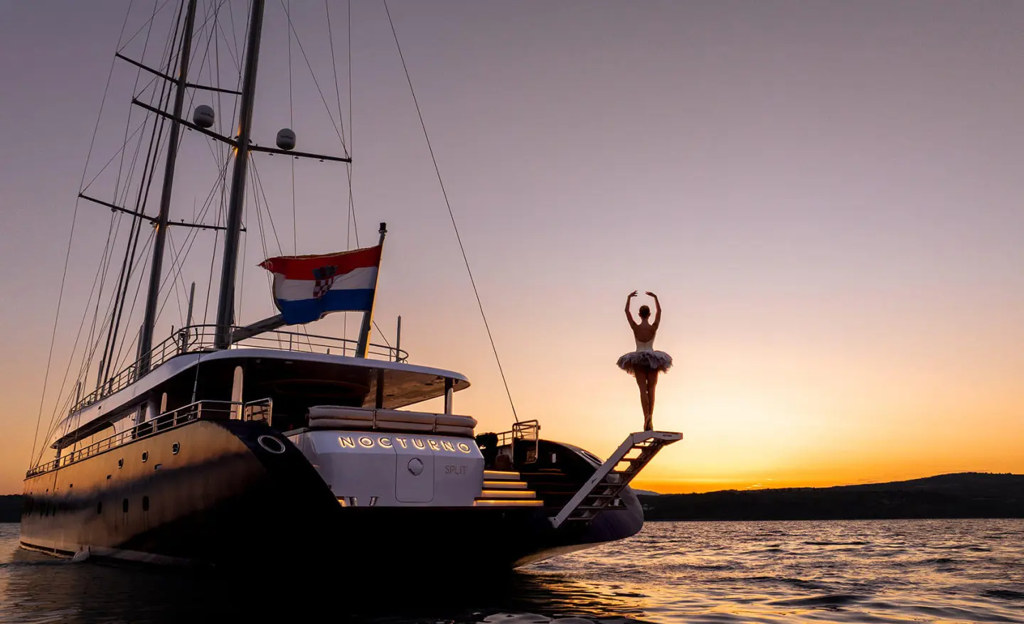 Nocturno yacht at sunset, silhouetted boat with mast against warm sky