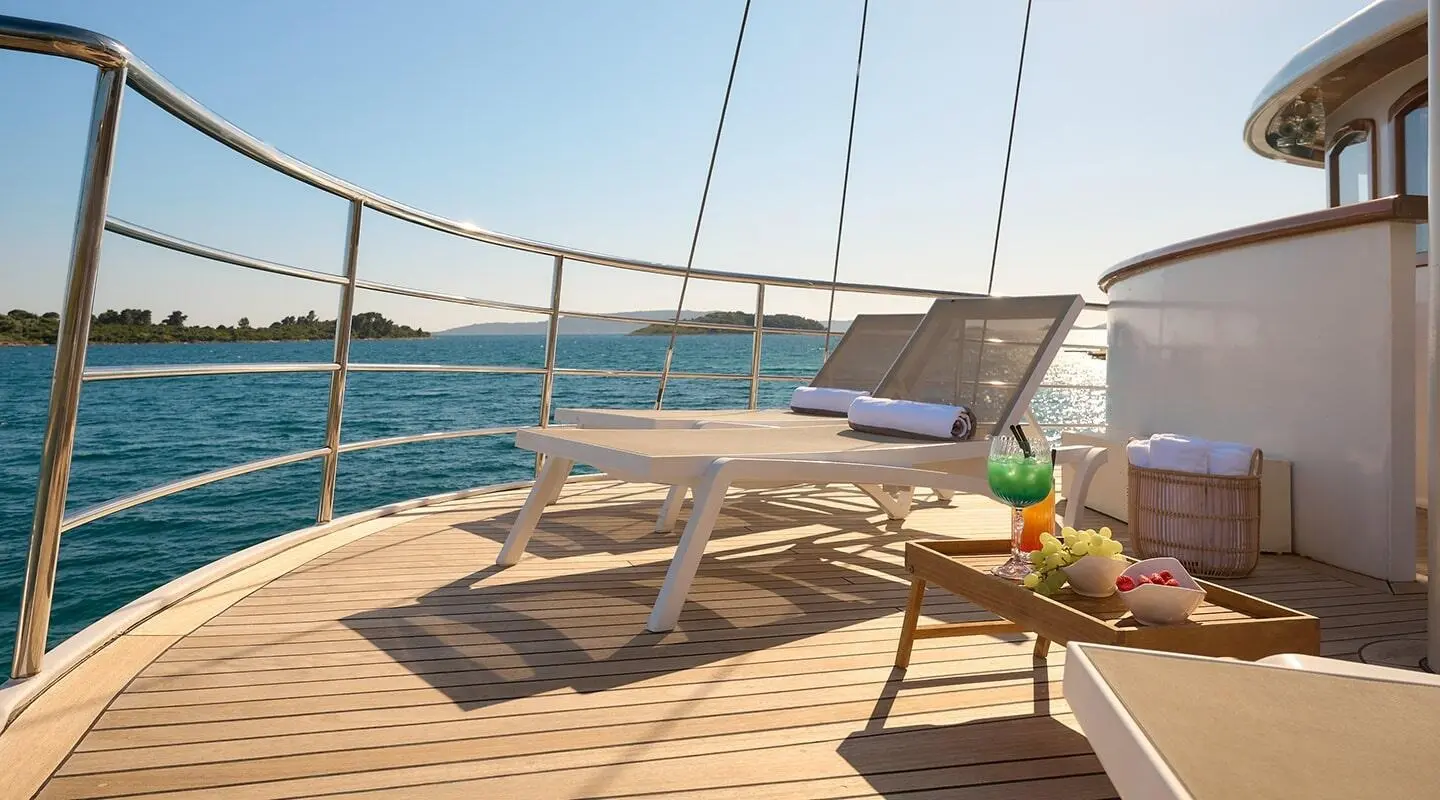 Deck of Bellezza luxury yacht with sun loungers, table, and ocean view