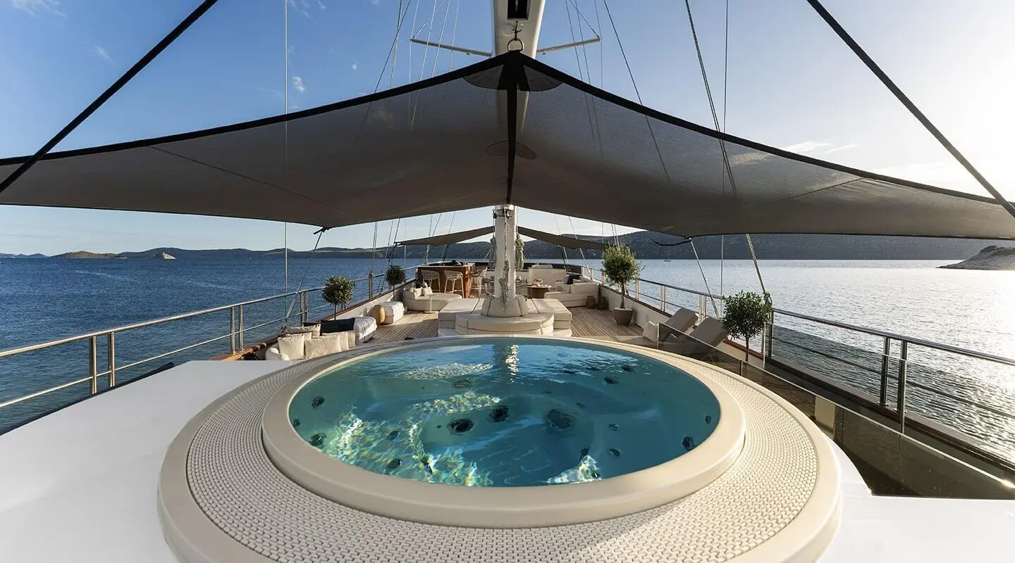 Maxita yacht deck with circular hot tub, sun loungers, and shaded seating at dusk