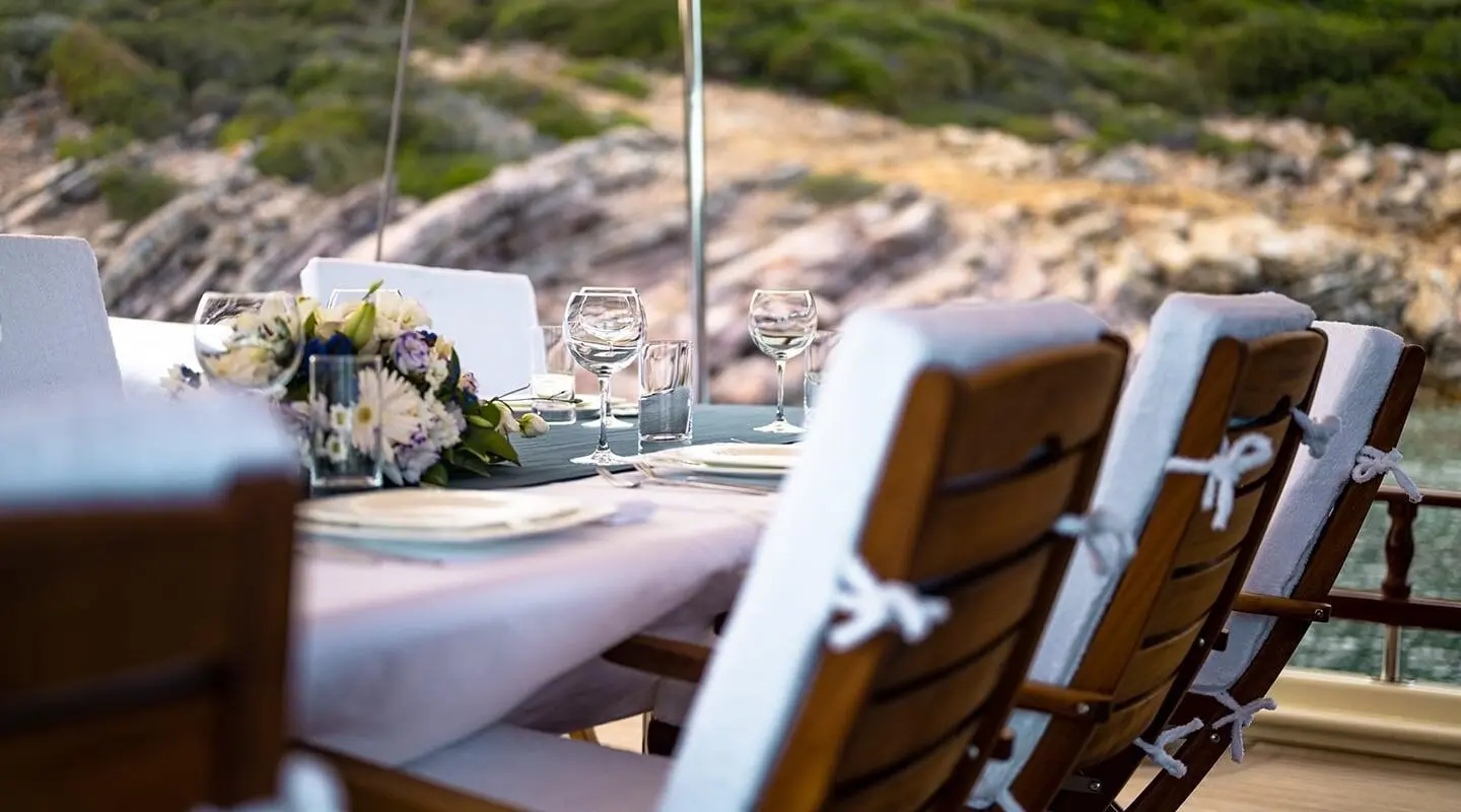 Luxurious yacht Estrella De Mar deck chairs on sunlit harbor rock backdrop at sunset