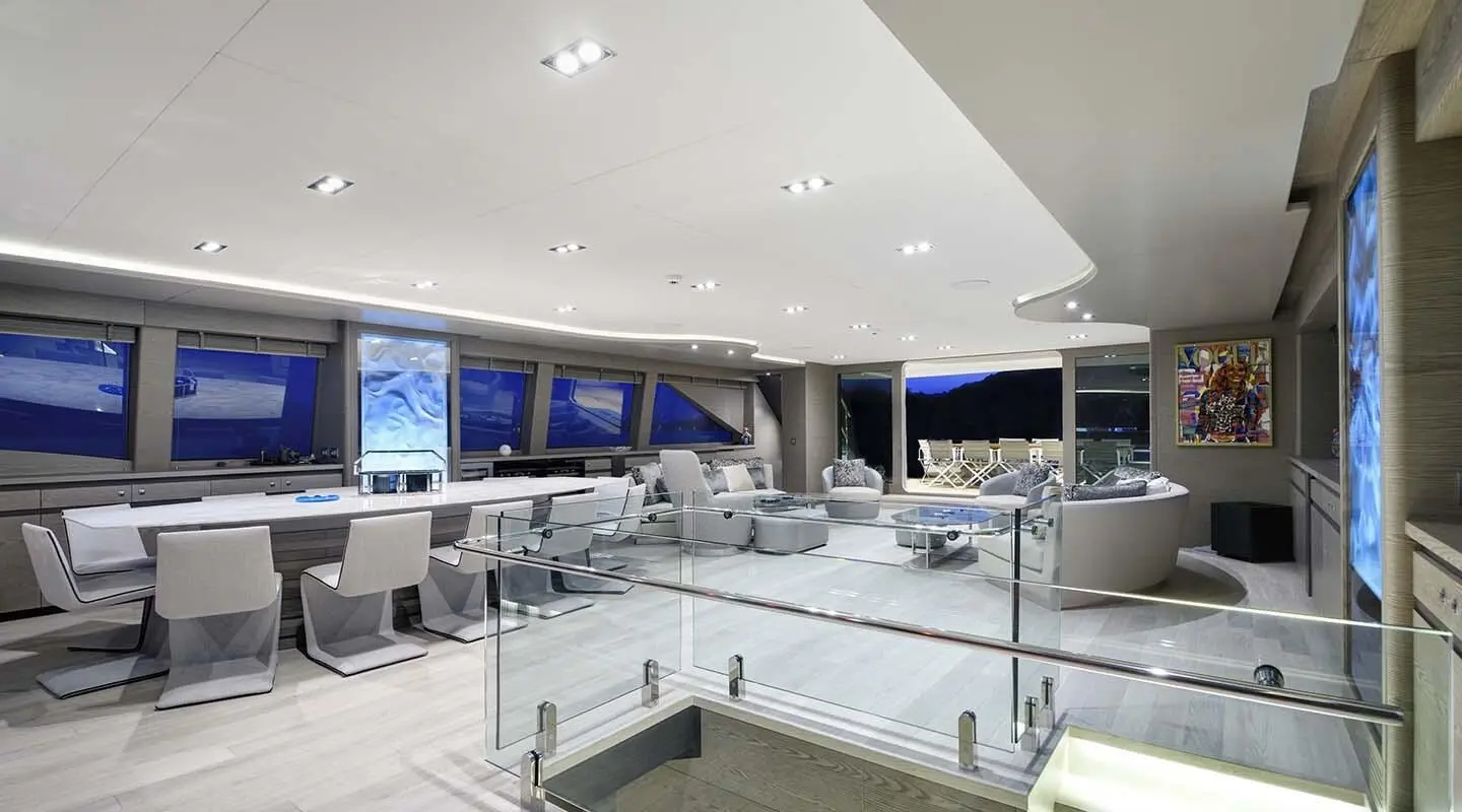 Interior yacht saloon with white seating, glass railings, and screens
