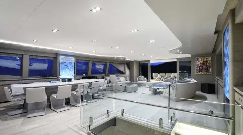Interior yacht saloon with white seating, glass railings, and screens