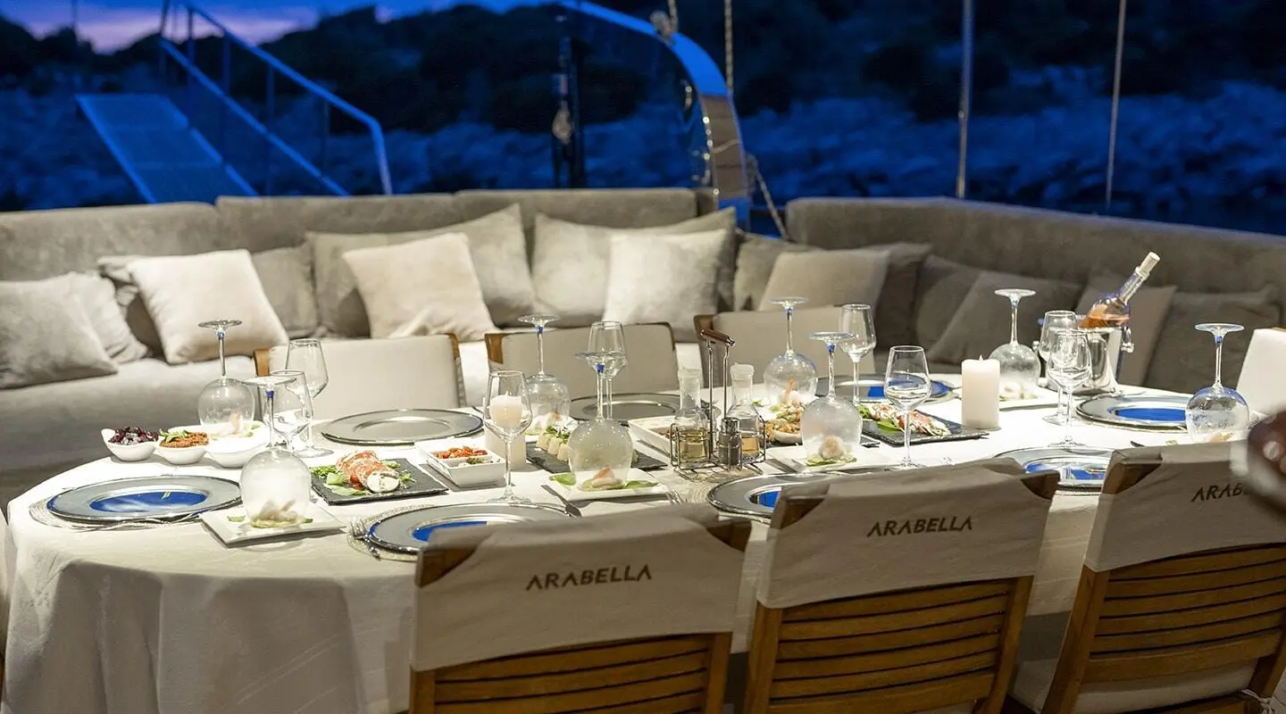 Arabella yacht dining setup on deck with white cushions and sunset ambiance