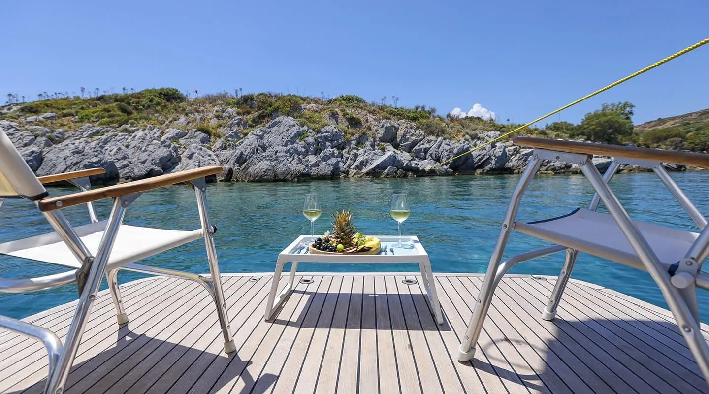Gazella yacht deck view facing calm sea, rocky coastline on the horizon