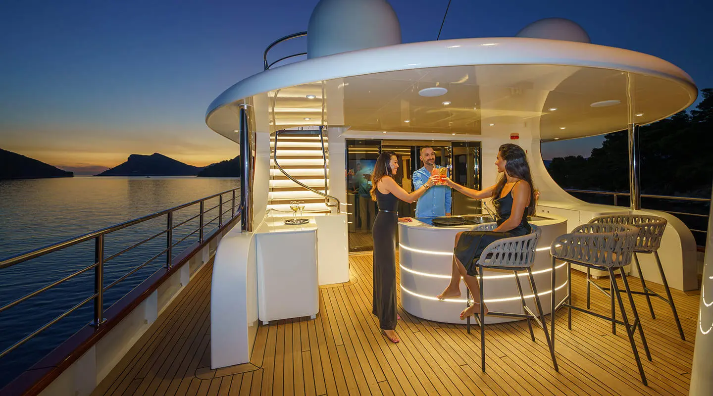 Maia yacht at dusk on deck with guests toasting at a curved bar