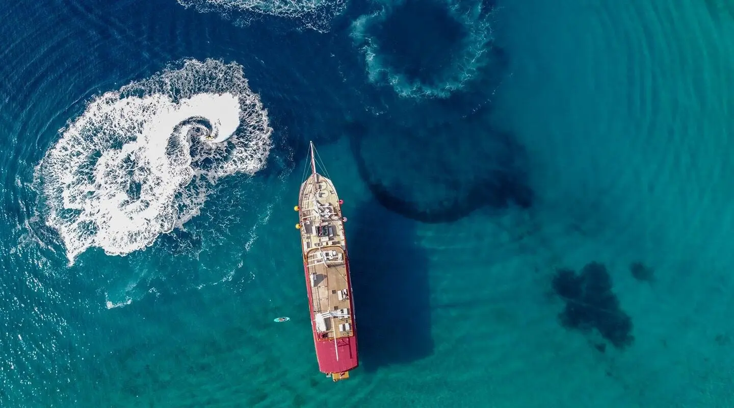 A red and white luxury motor yacht named Amorena sails in clear blue sea from aerial view