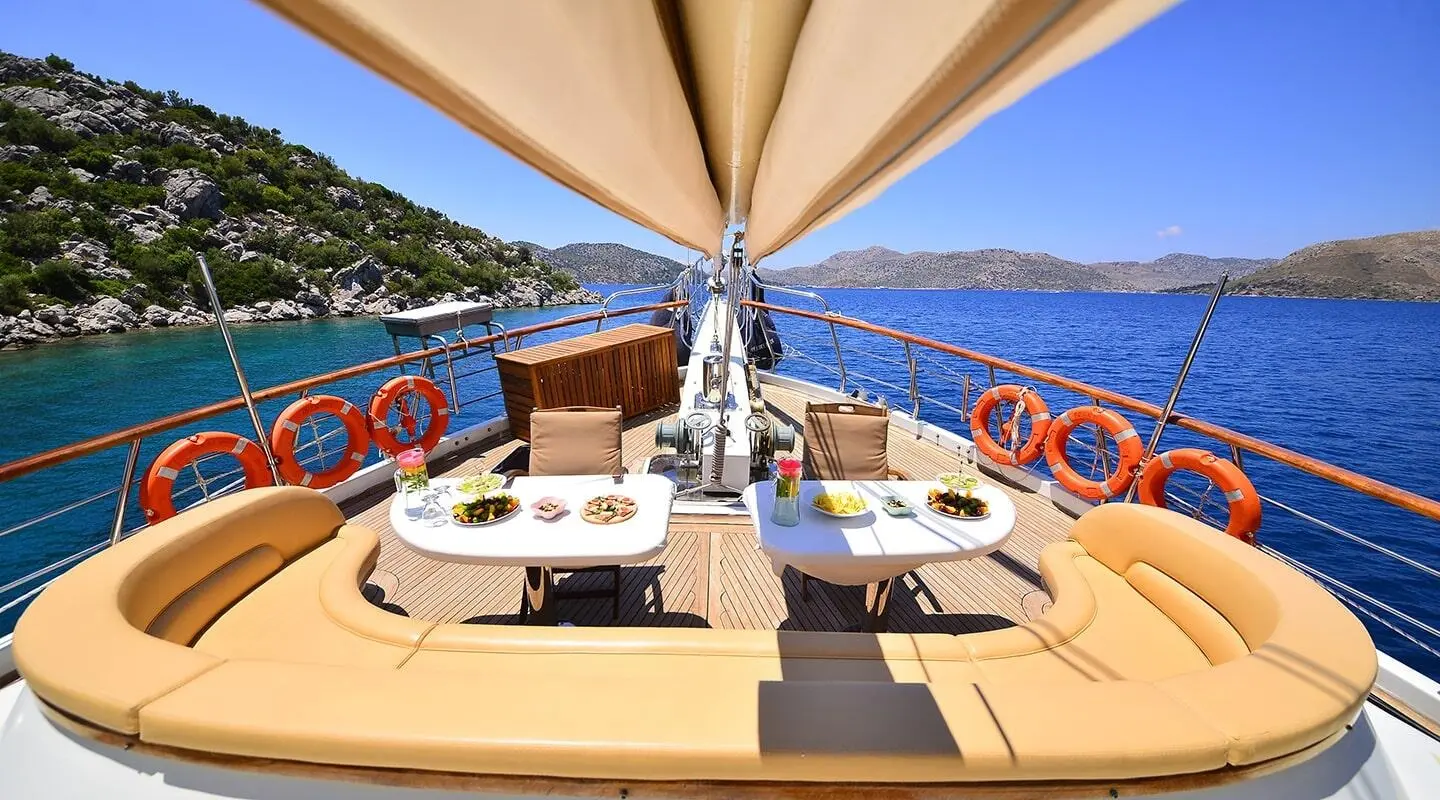 Sunlit yacht deck with seating and lifebuoys under a large sunshade on calm blue sea