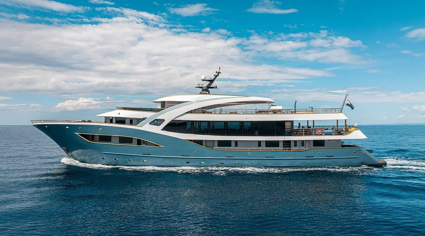 Bella luxury yacht anchored by calm blue water under cloudy sky