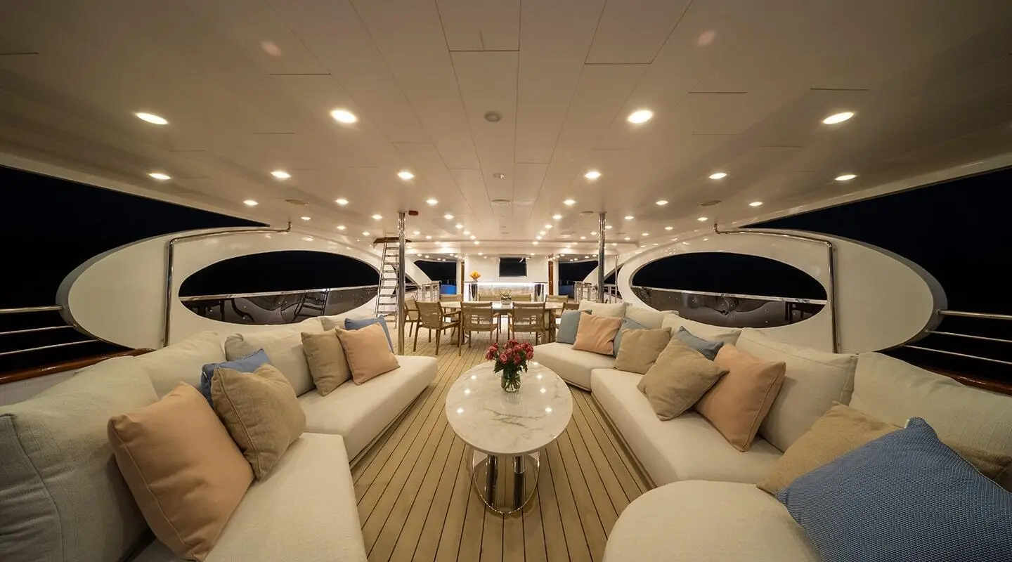 Open deck lounge with cushioned sofas, pastel pillows, and a marble central table