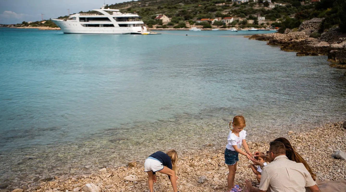 Karizma yacht exterior on calm sea near rocky shore with people on beach