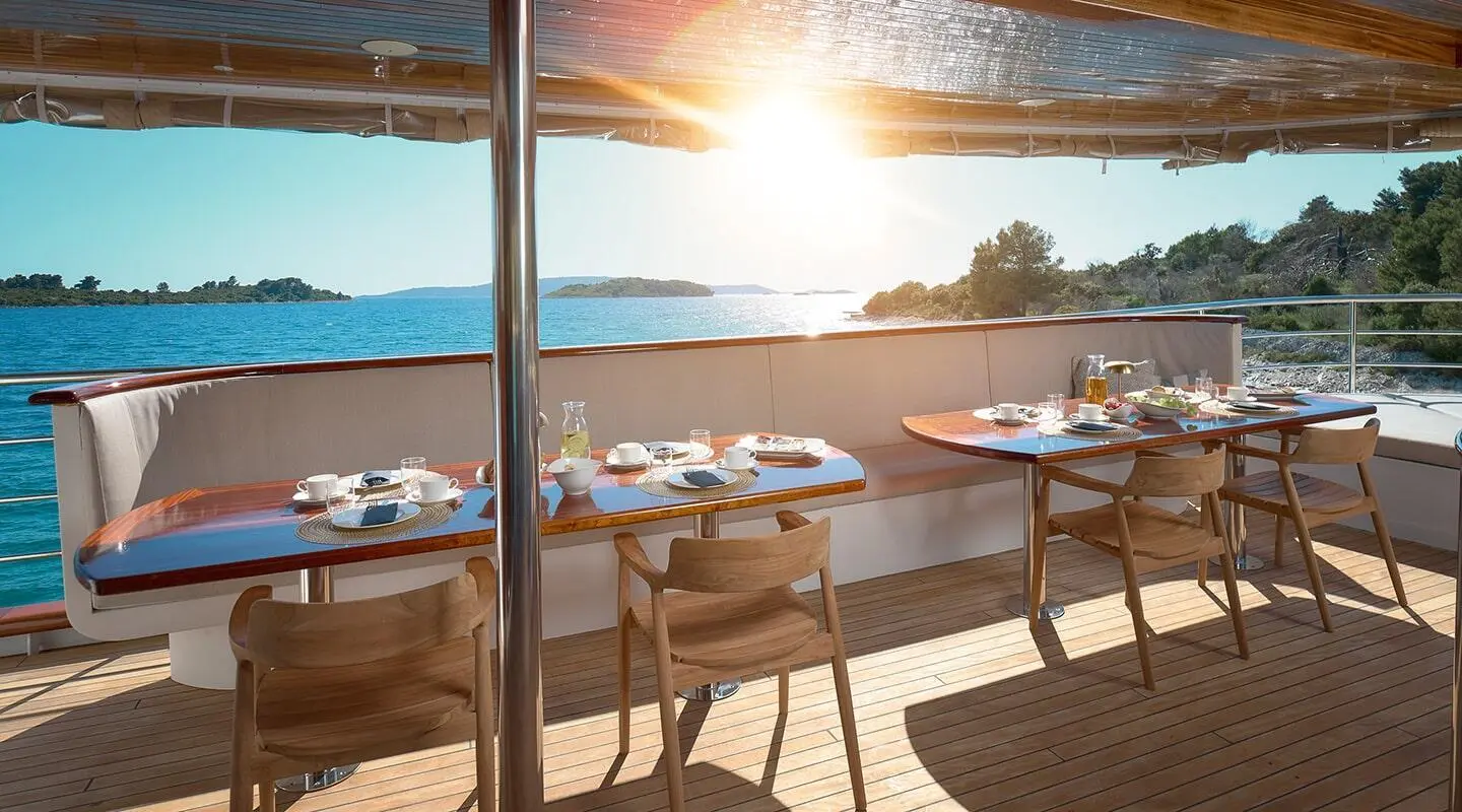 Bellezza yacht deck dining area with a sunlit table setup and ocean view