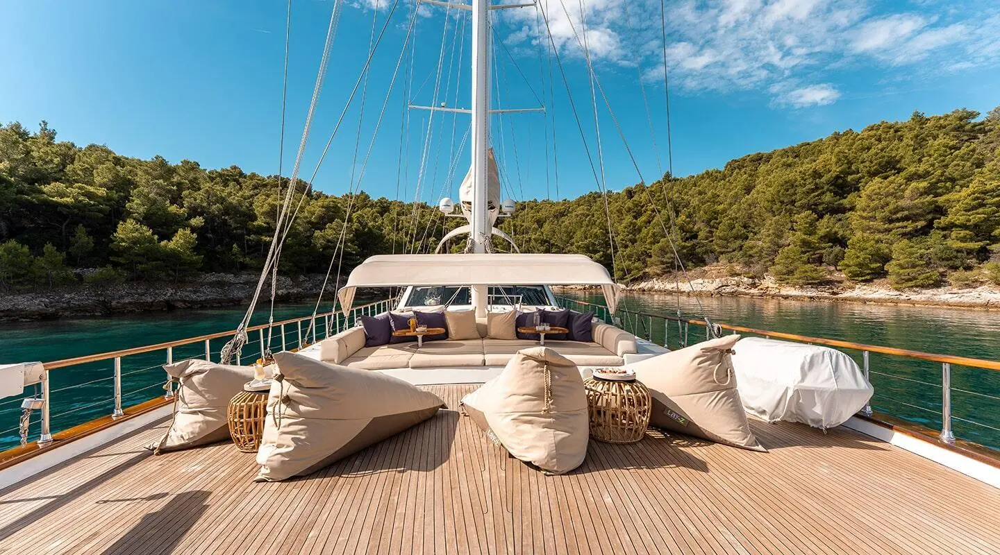 View of the deck with large seating and pillows, green forested shore and blue water