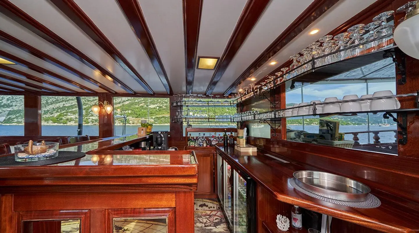 Wooden bar counter with shelves and glassware, sea and shoreline view in the background