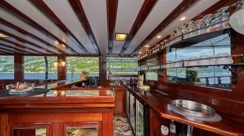 Wooden bar counter with shelves and glassware, sea and shoreline view in the background