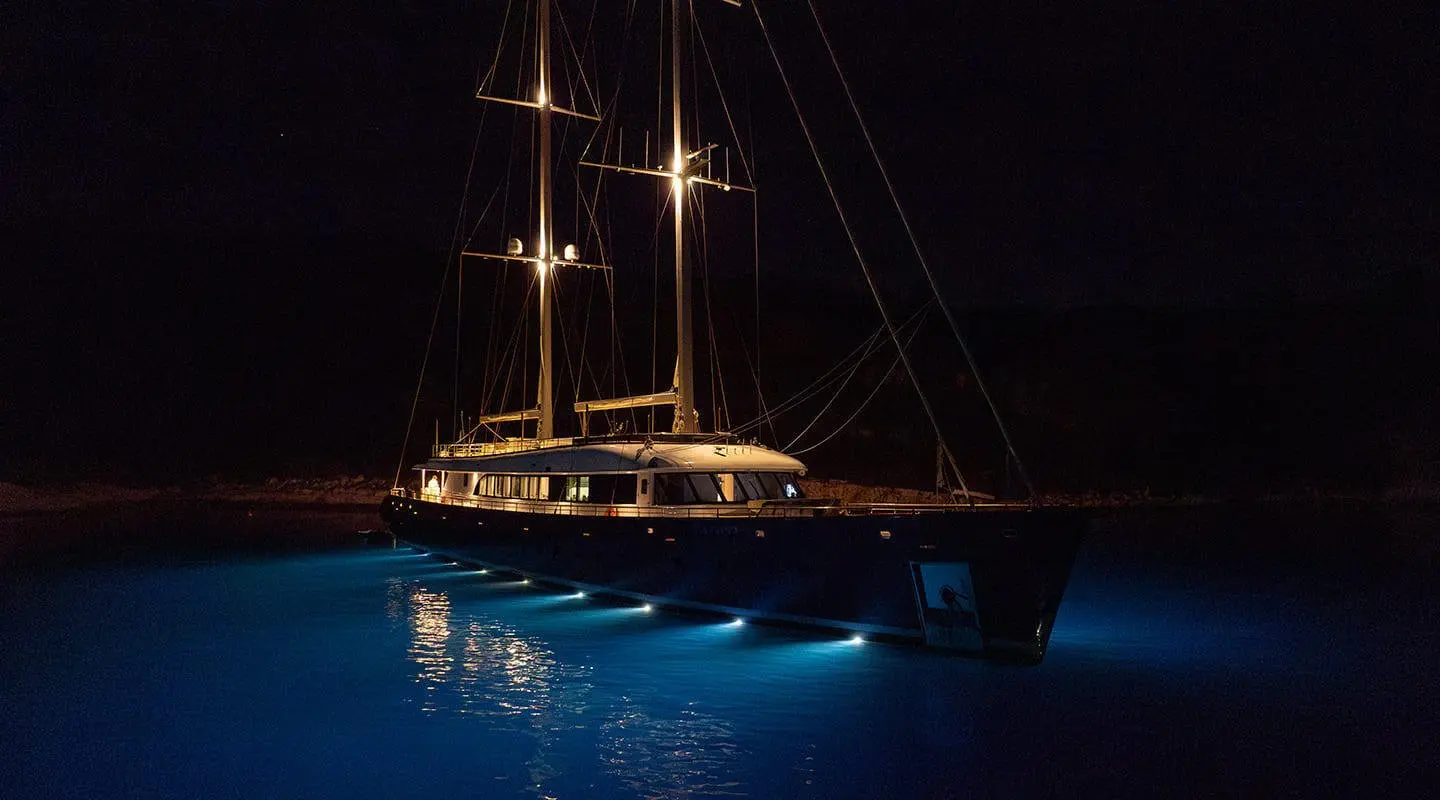 Nocturno sailing yacht at night, illuminated deck and dark water glow