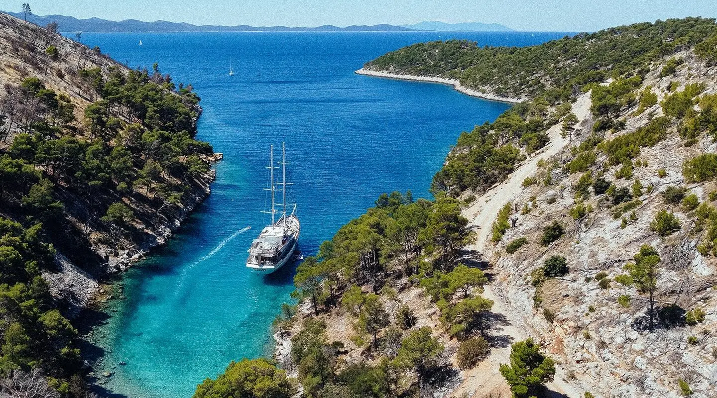 A 48m gulet yacht moored in a narrow rocky canyon with clear blue water