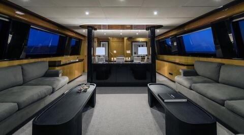 Luxurious 35.60m yacht interior: spacious salon with grey sofas, black coffee tables, ample windows, and a glossy black galley in the background