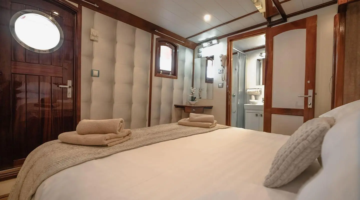 Mendula gulet interior with double cabin, beige cushions, wooden paneling, bed, and window view