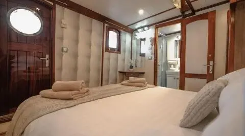 Mendula gulet interior with double cabin, beige cushions, wooden paneling, bed, and window view