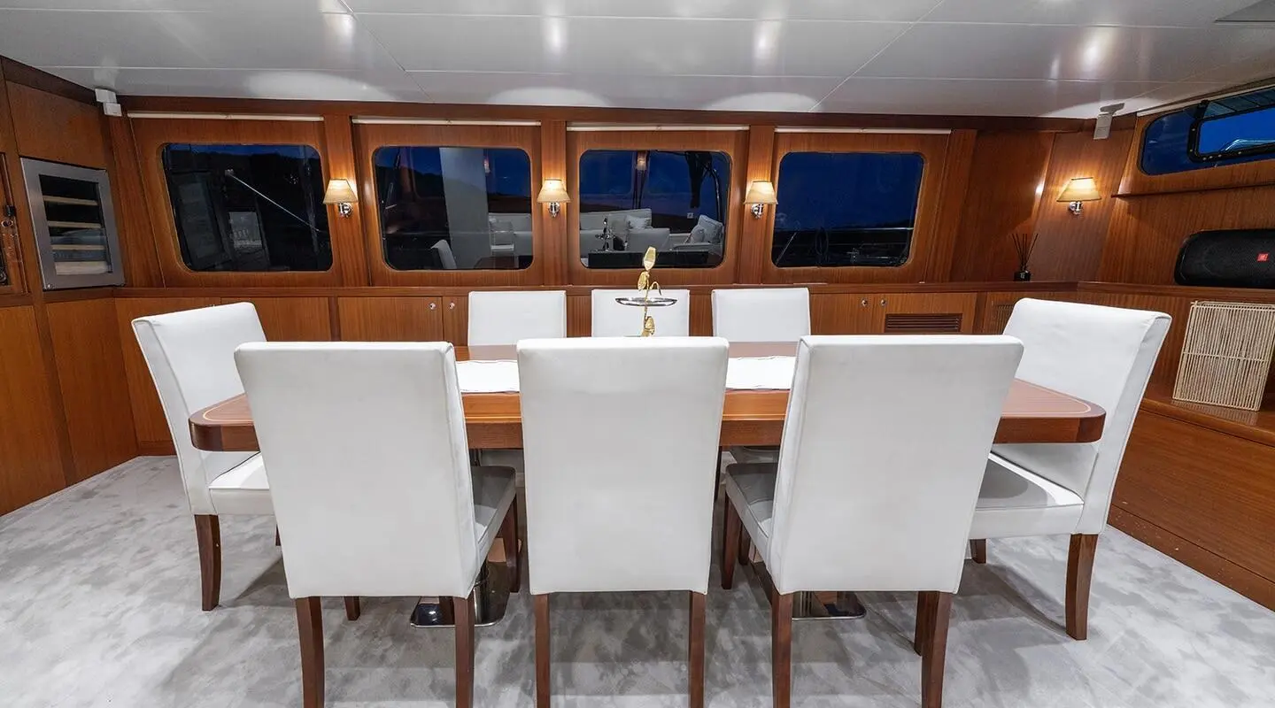 Sailing yacht Lucky You interior with wooden panels, white seating, and windows at sunset