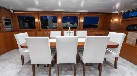Sailing yacht Lucky You interior with wooden panels, white seating, and windows at sunset