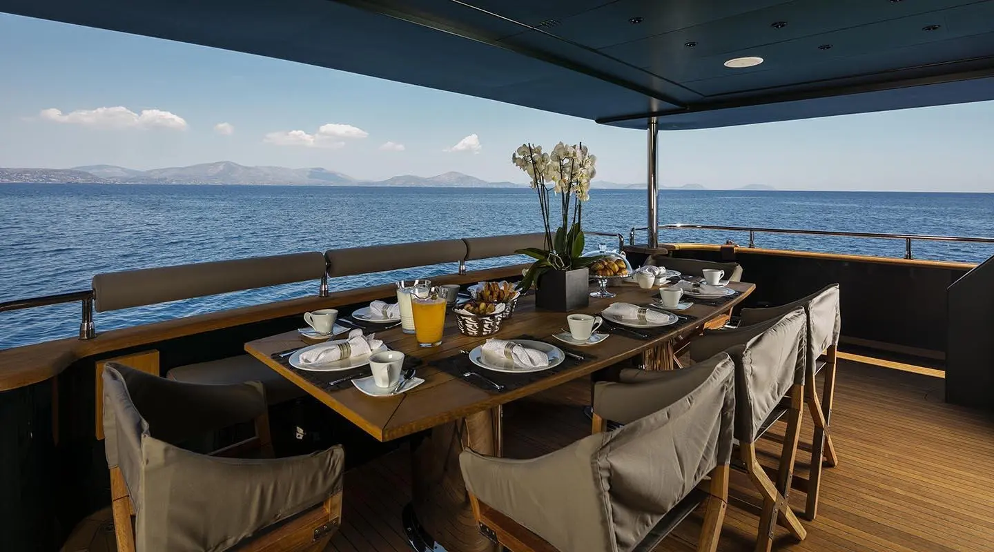 Yacht dining area on deck with table settings and chairs under canopy, ocean view