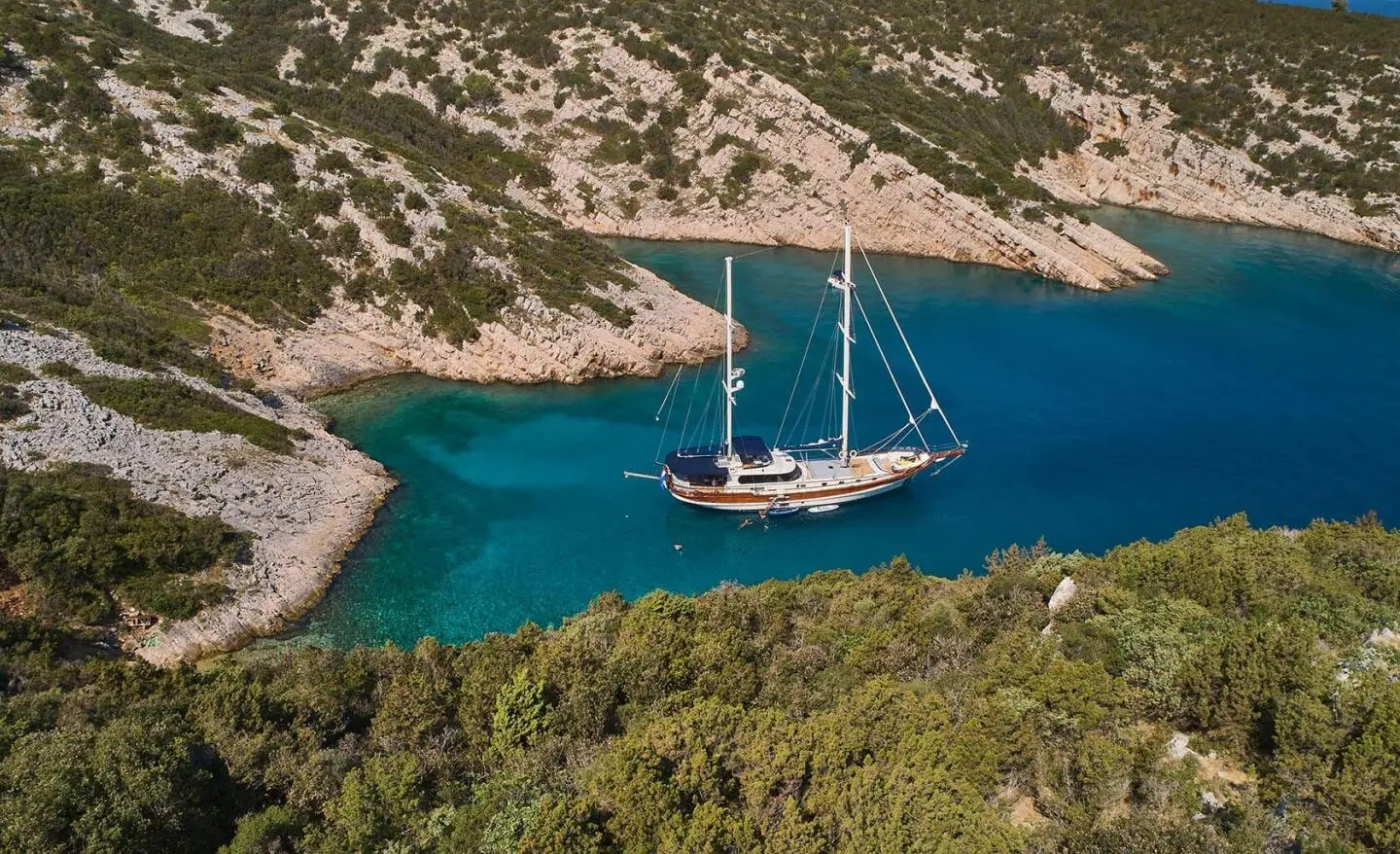 Lotus yacht anchored in a cove with clear blue water and rocky coastline