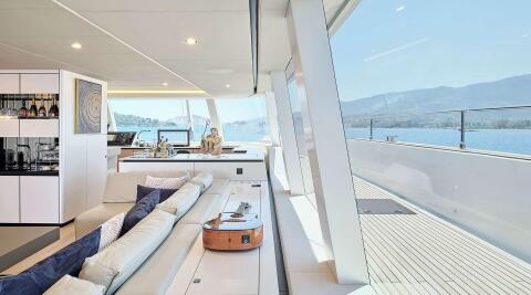 Genny luxury yacht interior: open-plan salon with white seating, bar, and guitarist guitar on ottoman, large panoramic windows over calm sea