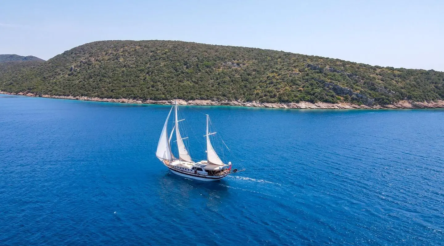 Ulucinar sailing yacht with white sails cruising azure seas near rugged coastline