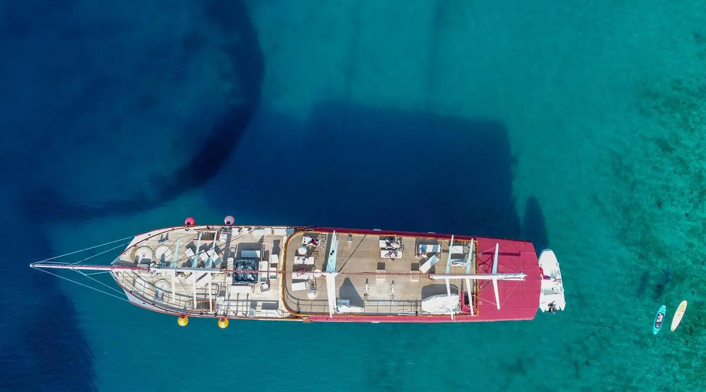 Amorena yacht seen from above with red aft, wooden deck and seating areas on turquoise sea