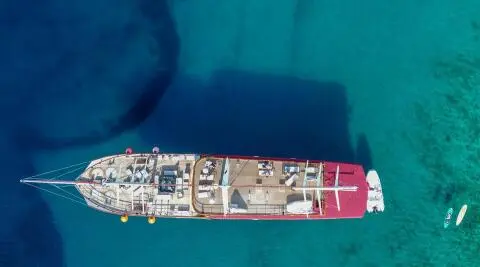 Amorena yacht seen from above with red aft, wooden deck and seating areas on turquoise sea