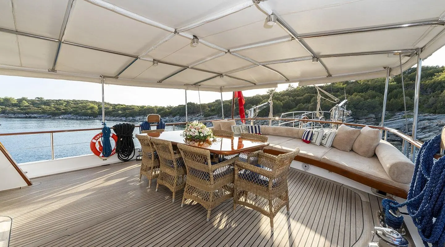 Artemis luxury yacht deck with wooden dining table and seating under a canopy at sunset