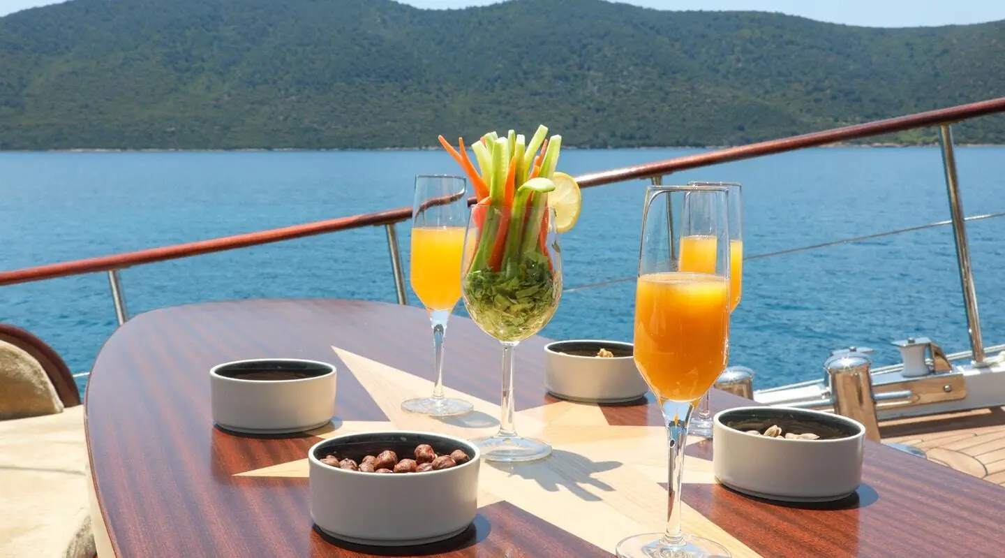 Yacht Ulucinar charter deck with tropical drinks, ocean horizon sunset glow