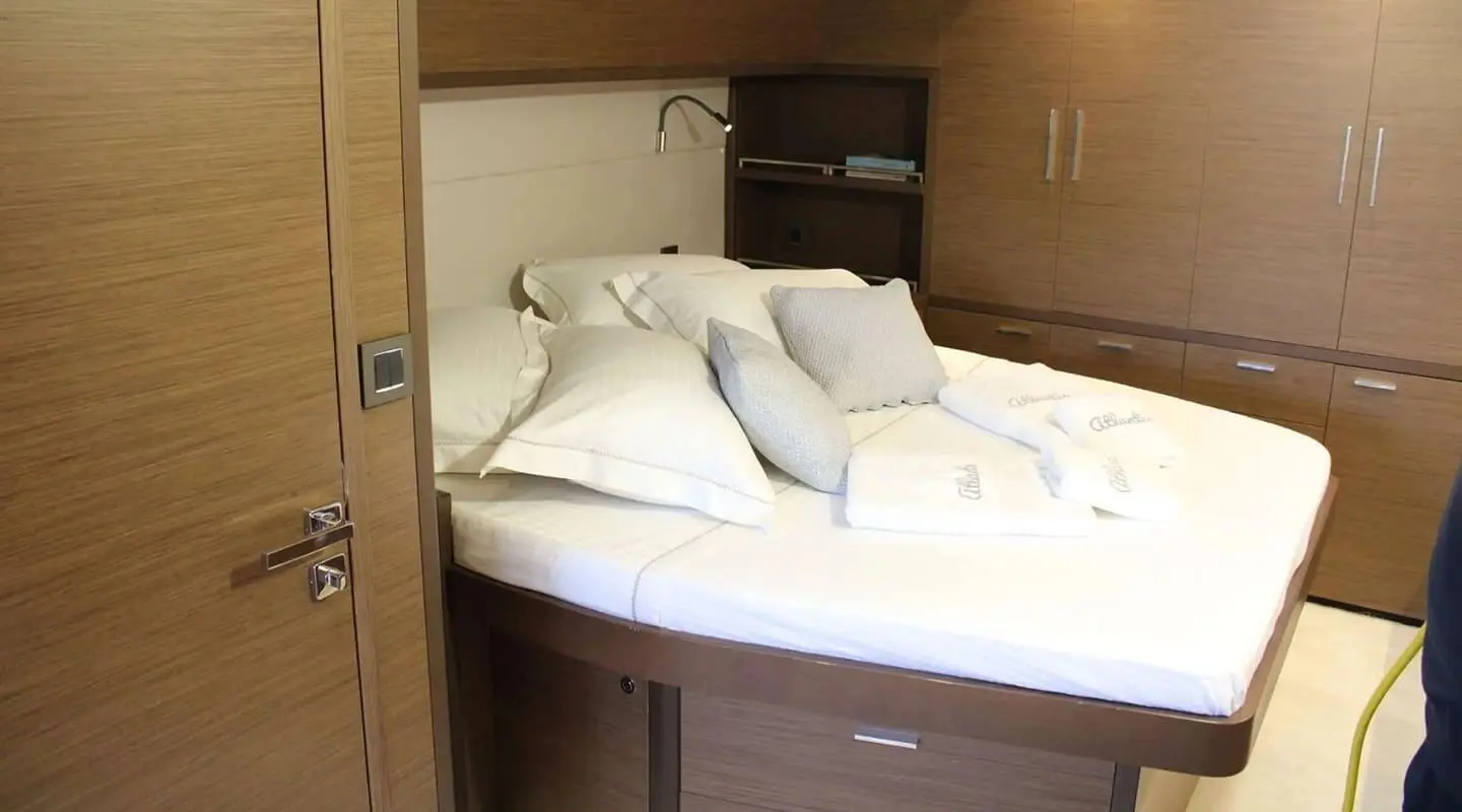Luxurious yacht interior cabin with large bed, white linens, wooden cabinetry