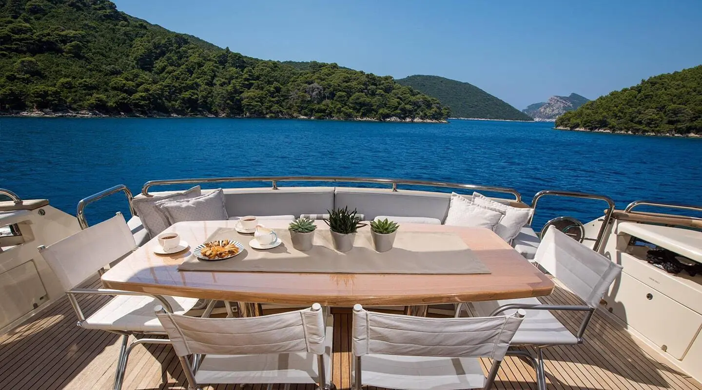 Salt yacht outdoor dining on deck with wooden table and white seating overlooking blue sea