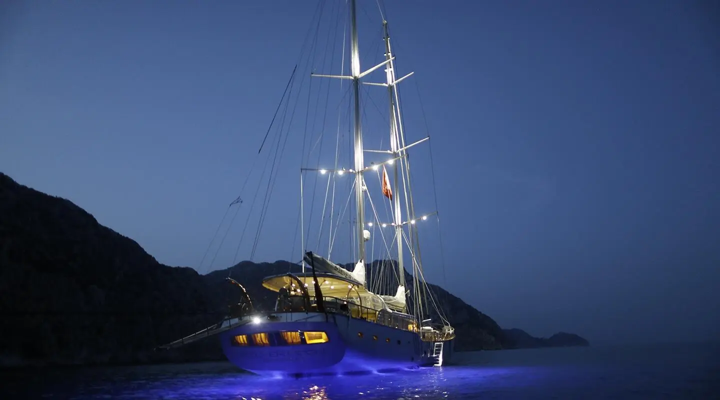 Yacht Silver Moon at night with illuminated hull and tall mast on calm dark water