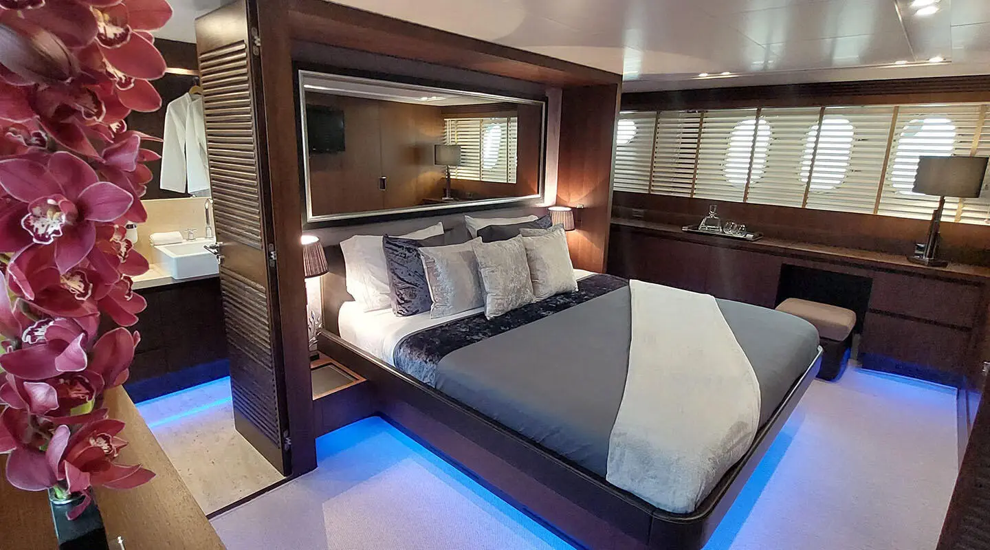 Miraval yacht bedroom with bed, blue lighting, dark wood cabinets