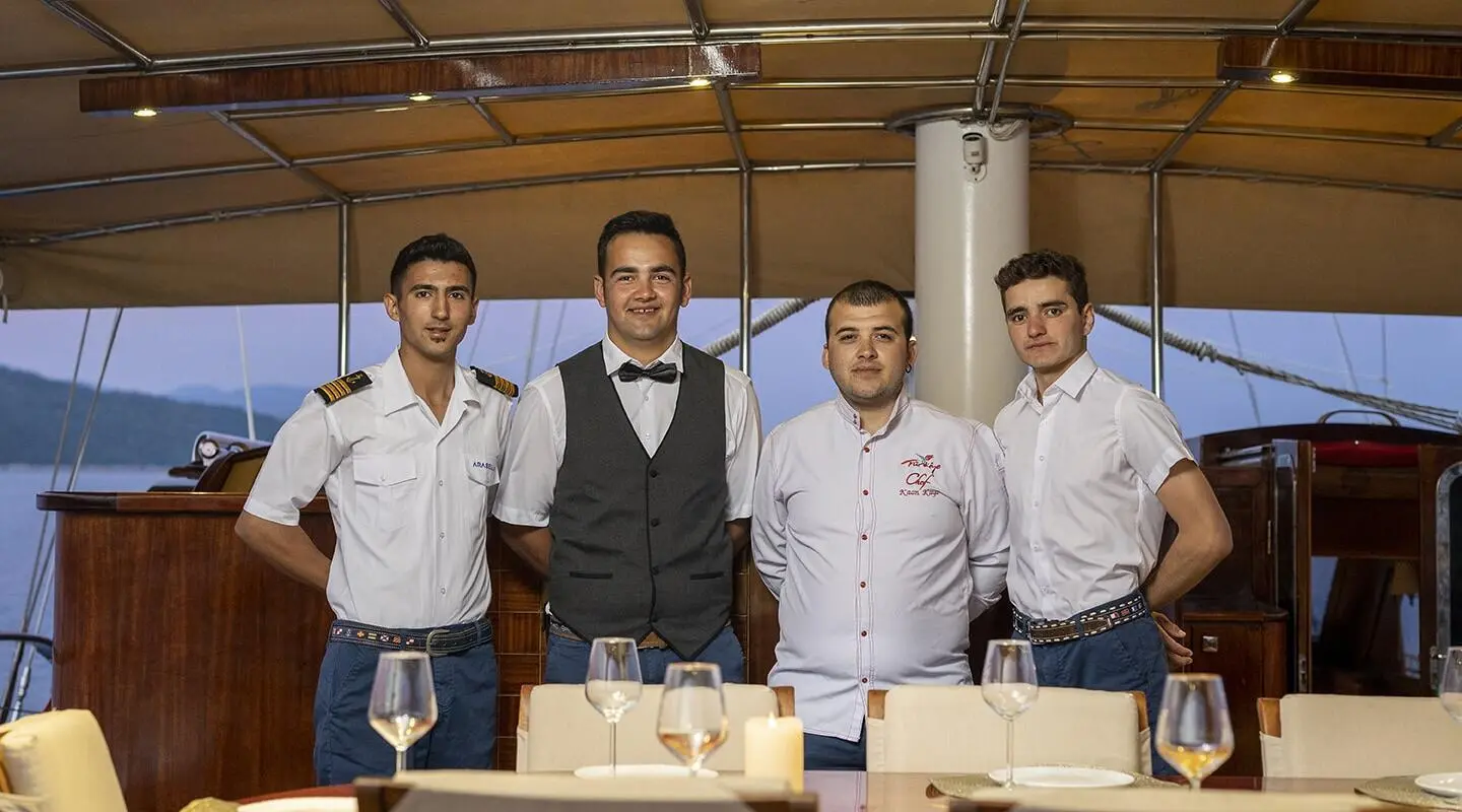 Arabella yacht crew seated at table on deck during sunset with sails nearby