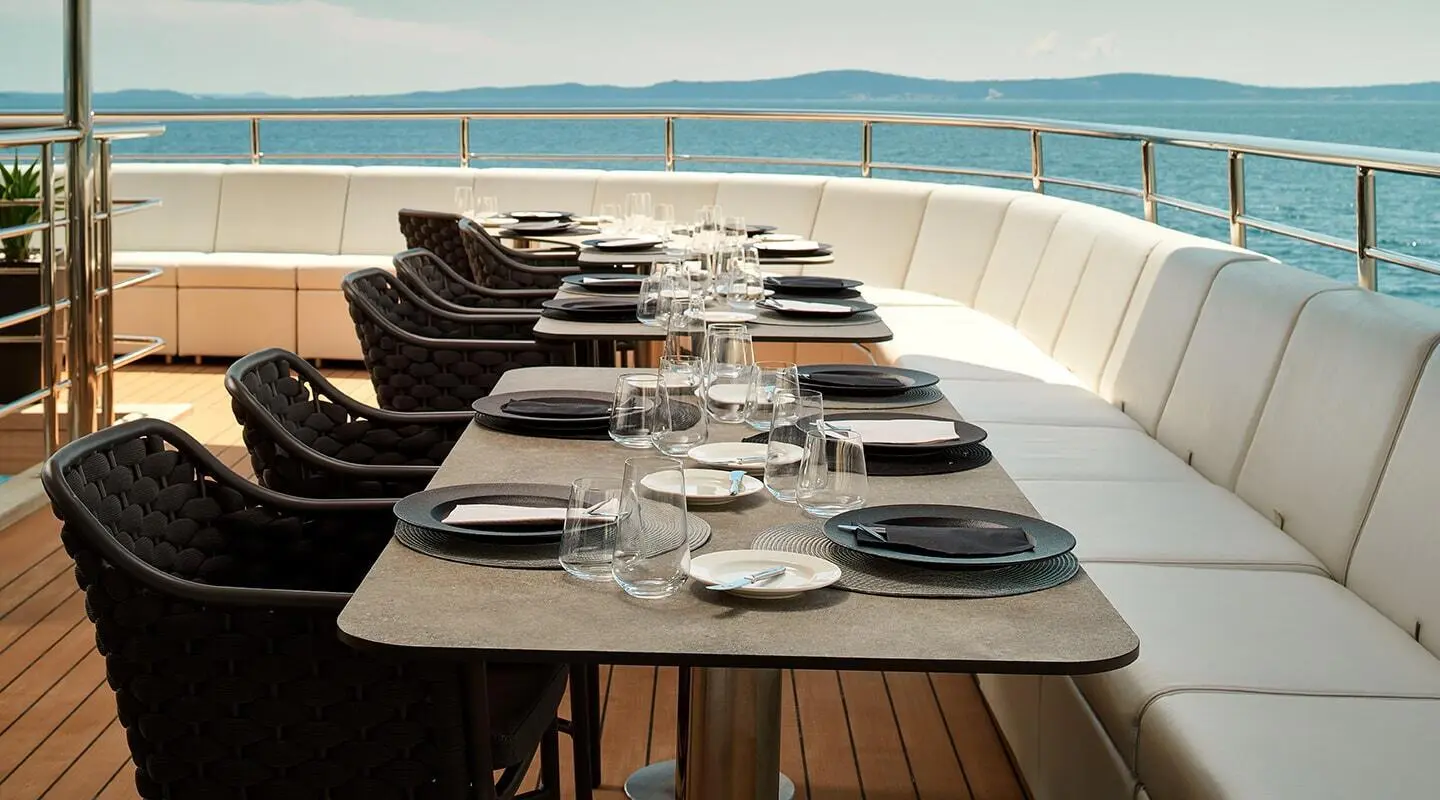 Table on Ohana yacht with plates, cutlery, and decorative items overlooking water