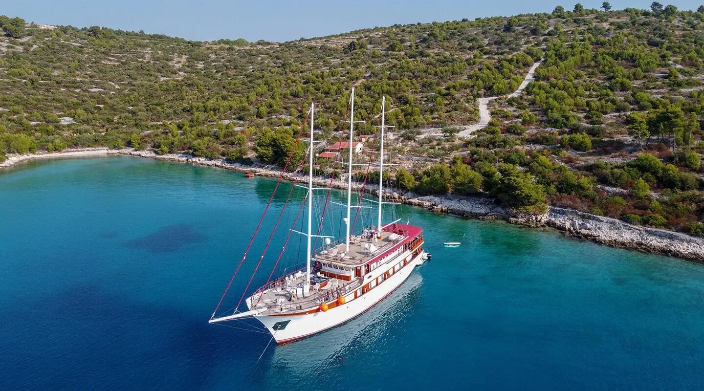 A white sailing yacht named Amorena anchored near rocky coastline under clear blue sky