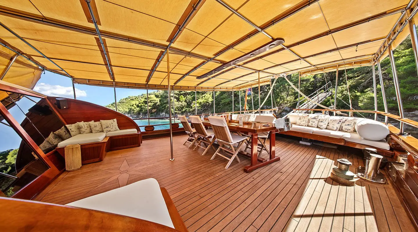 Elegant yacht deck with wooden floor, canopy, seating, and dining area at sunset