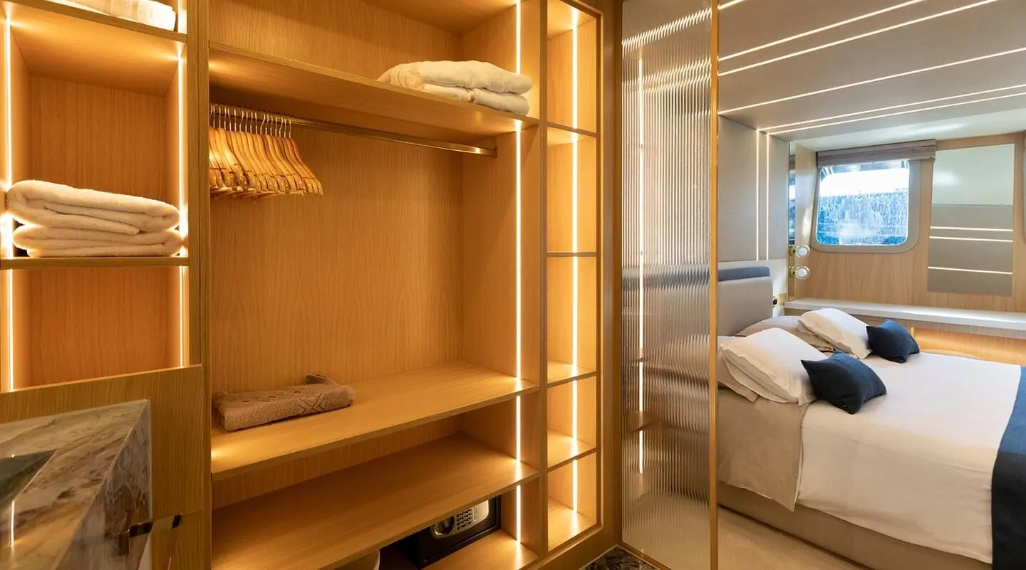 Walk-in wardrobe and bedroom area with wooden shelves and illuminated sections
