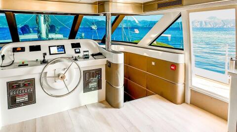 Angelo III yacht helm station with wheel and navigation screens aboard, sea view through windows