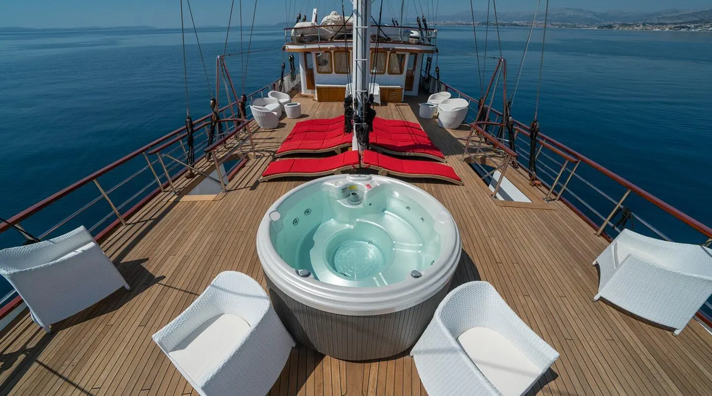 On a sunlit deck, red lounge beds and a large hot tub on a yacht deck